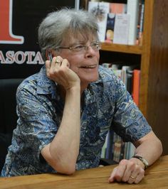 a woman sitting at a table talking on her cell phone in front of a bookshelf