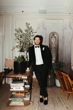 a man in a tuxedo standing next to a table with books on it