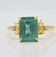 an emerald and diamond ring with yellow gold accents on a white background, showing the green stone surrounded by two diamonds