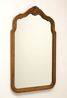 a wooden mirror hanging on the wall next to a white wall with an ornate frame