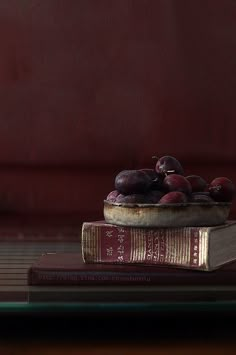 a bowl of plums sitting on top of two books