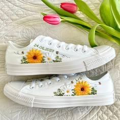 two white shoes with sunflowers painted on them next to pink tulips