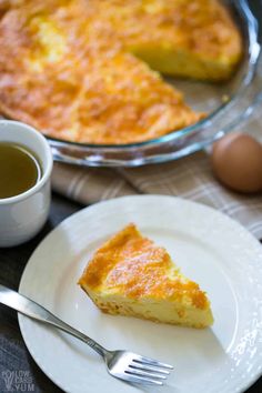 a piece of quiche on a plate next to a cup of tea and a fork