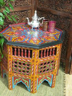 a colorful table with a tea pot on it and some plants in the corner next to it