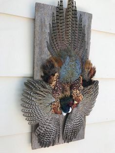 a wall mounted bird sculpture on the side of a white house, with feathers all over it's body