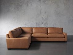 a tan leather sectional sofa sitting in front of a gray wall with concrete flooring