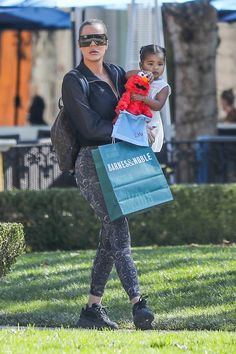 a woman carrying a child in her arms while walking through the grass with shopping bags