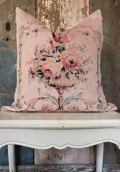 a pink floral pillow sitting on top of a white table next to a wooden wall