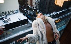 a woman standing on top of a building next to a street filled with traffic and buildings covered in snow