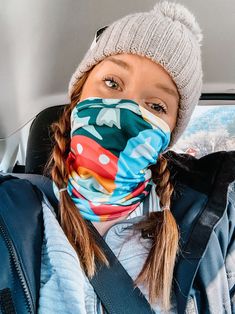 a woman wearing a scarf and hat in the back seat of a car with her face covered