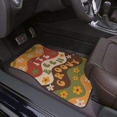 a car floor mat with flowers and the word good on it in front of a steering wheel