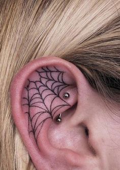 a woman's ear has a spider web tattoo on it