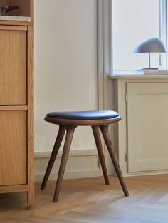 a wooden stool sitting in front of a window next to a cabinet and lamp on top of a hard wood floor