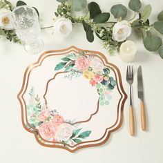 a place setting with flowers and greenery on the table, along with silverware