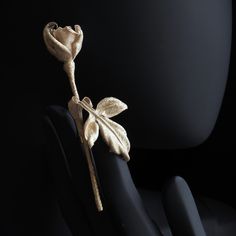 a gold rose is on top of a black object with two hands and one hand holding it