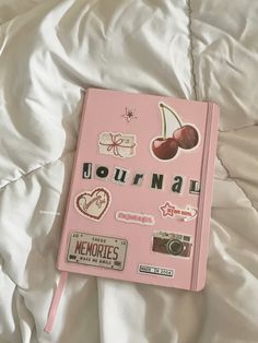 a pink notebook with stickers on it sitting on a bed covered in white sheets