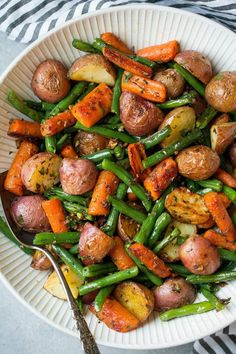 a white bowl filled with potatoes, green beans and carrots next to a fork