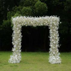 a white flower covered archway in the middle of a field