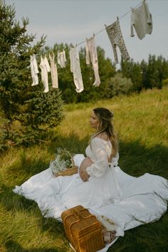 a woman sitting in the grass with clothes hanging above her