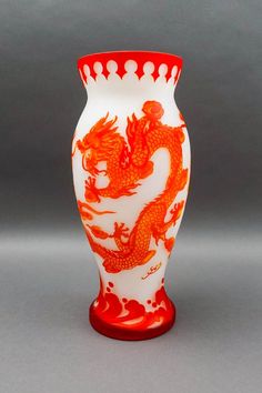 a red and white vase sitting on top of a gray table next to a wall