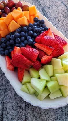 a platter filled with sliced fruit on top of a granite counter next to a bowl of grapes, strawberries, and melon