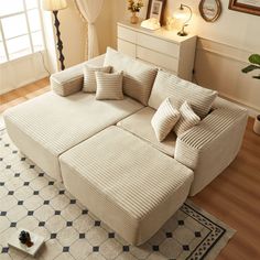 a living room with a large sectional couch and pillows on the floor next to a window