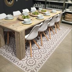 a wooden table topped with white chairs next to a shelf filled with plates and bowls