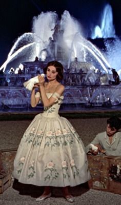 a woman standing next to a man in front of a fountain