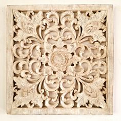 an intricately carved wooden panel with leaves and flowers on the center, mounted on a white wall