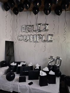 the table is set up with balloons and black boxes on it, which read feliz cumple