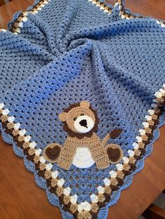 a blue crocheted blanket with a brown teddy bear on it sitting on top of a wooden table