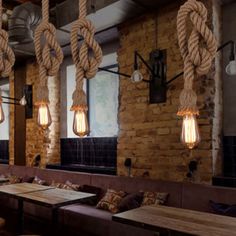 an industrial style restaurant with rope hanging from the ceiling and wooden tables in front of them