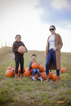 a woman and two children with pumpkins on the ground in front of an open field