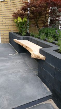 a wooden bench sitting on top of a cement slab next to flowers and trees in front of a brick building