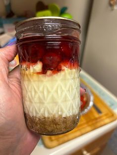 a person holding a mason jar filled with fruit and yogurt on top of a counter