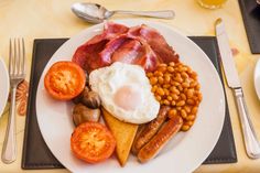 a white plate topped with eggs, bacon and tomatoes next to other foods on a table