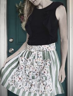 a woman standing in front of a green door wearing a skirt with flowers on it