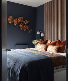 a bedroom with dark blue walls and orange pillows on the bed, along with decorative wall hangings