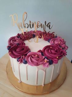 a white cake with pink flowers and gold lettering on top is sitting on a wooden table