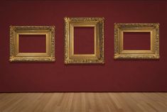 three gold frames on a red wall in an empty room with wood floor and wooden floors