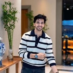 a man is standing in front of a vase and looking at the camera with a smile on his face