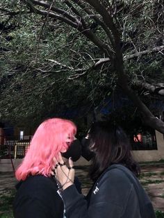 two women with pink hair are kissing under a tree