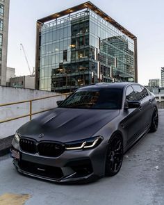 a grey bmw car parked in front of a large building with glass windows on it