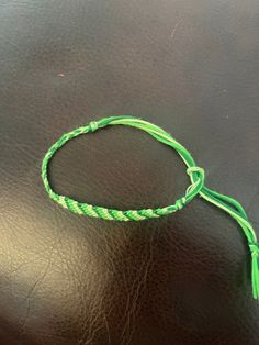 a green string bracelet on a leather surface