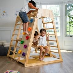 two children playing on a wooden climbing frame in a room with hardwood floors and windows