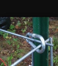 a close up of a chain link on a green pole with grass and trees in the background