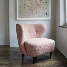 a pink chair sitting in front of a window next to a painting on the wall