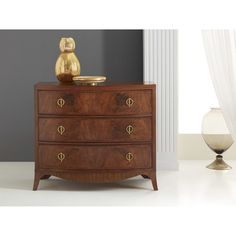 a wooden chest of drawers sitting on top of a white floor next to a vase