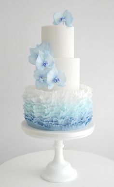 a three tiered cake with blue flowers on top and white frosting around the edges