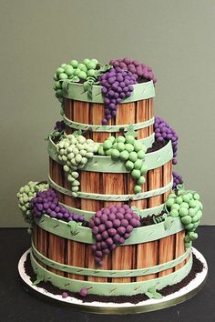 a three tiered cake decorated with grapes and bamboo strips on top of a black table